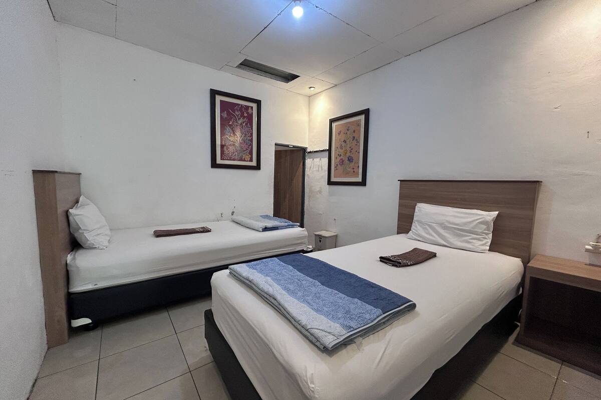 A hotel room with two beds, a wooden headboard, a nightstand, and two framed pictures on the wall.