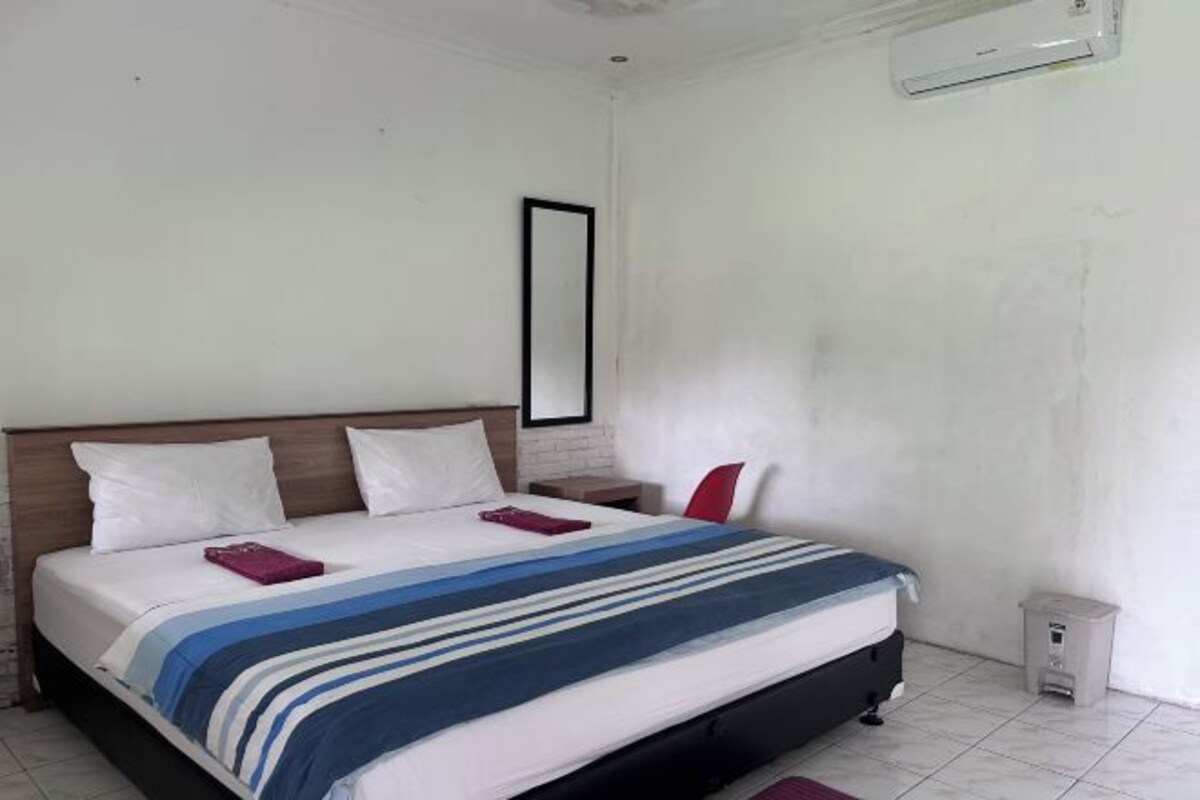A neatly made bed with a striped bedspread, a wooden headboard, and a small bedside table with a red pillow.