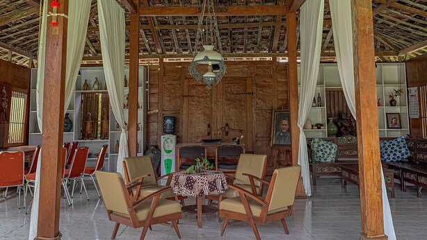 Un espacio de estar al aire libre cubierto, con pilares de madera, suelo de baldosas y una mesa central con sillas.