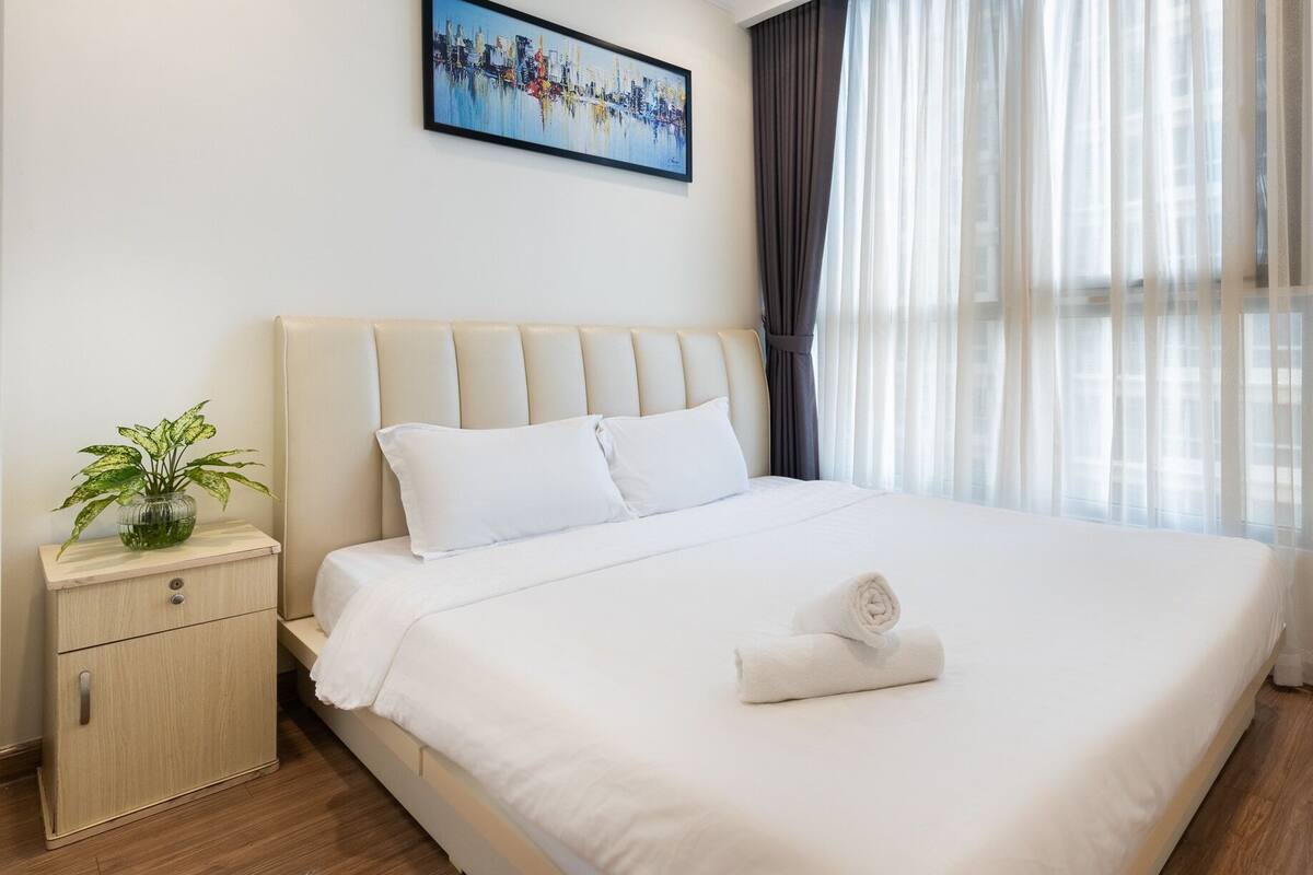 A hotel room with a large bed, a nightstand with a plant, and a painting on the wall.