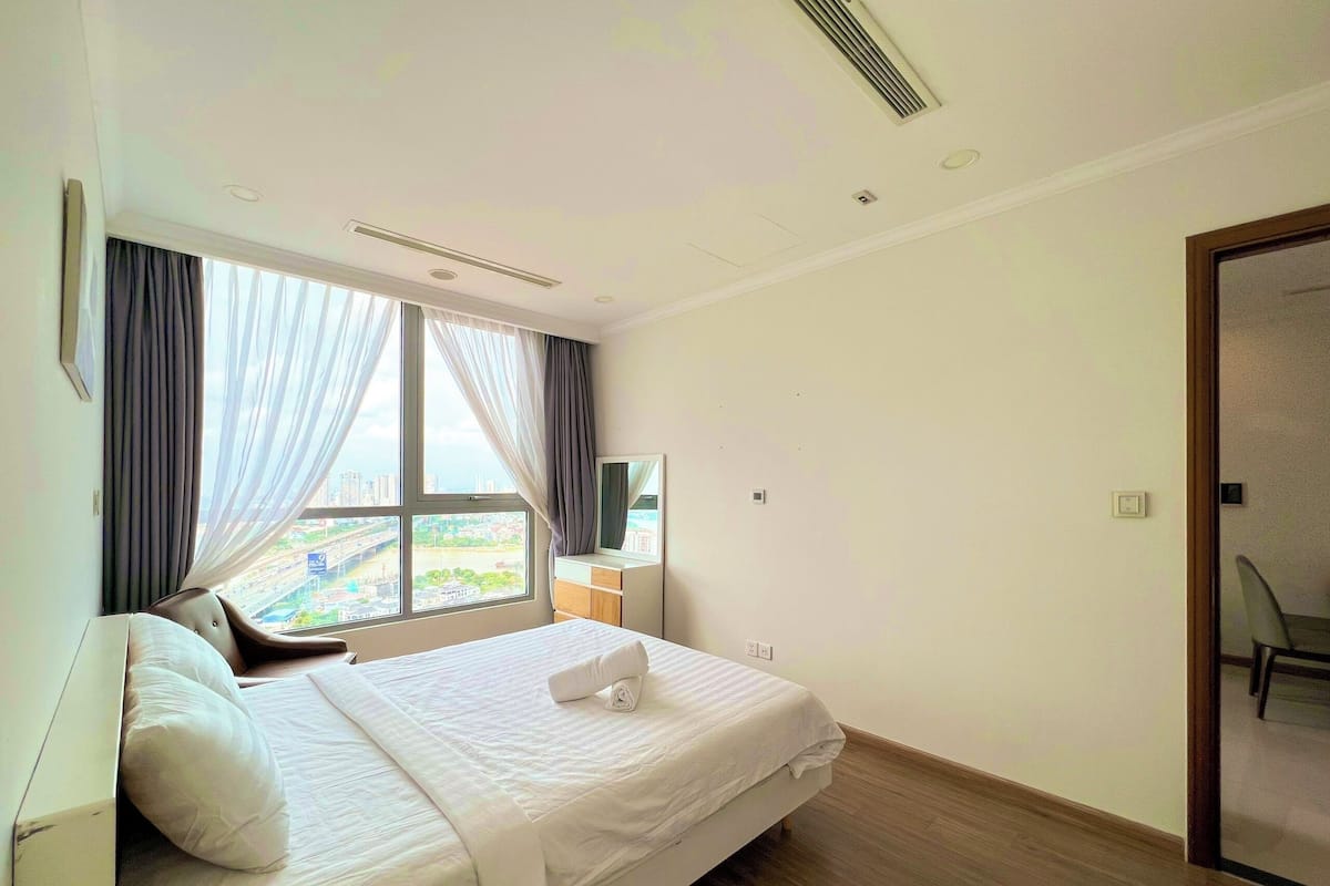 A hotel room with a bed, a window with curtains, a wooden floor, and a door.