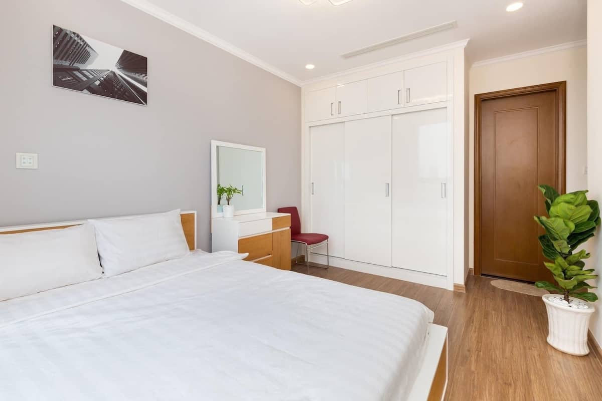 A bedroom with a bed, a wardrobe, a mirror, a red chair, and a potted plant.