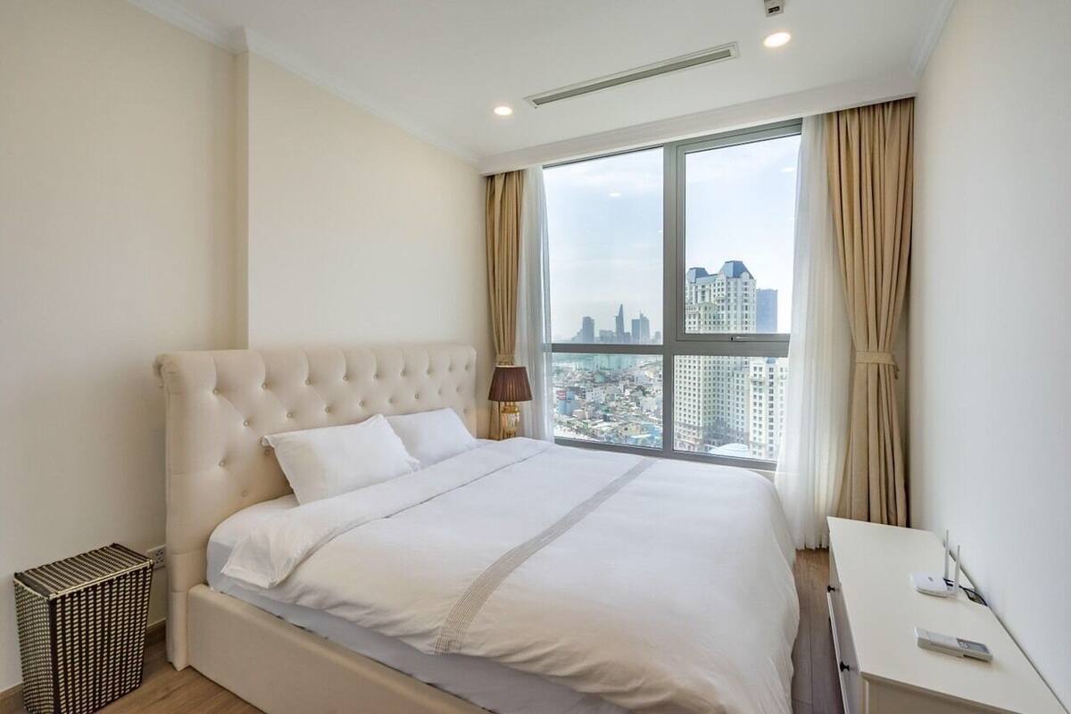 A hotel room with a large bed, a desk, and a view of a cityscape through a large window.