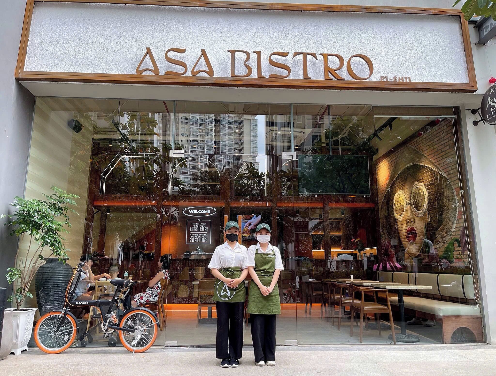 Exterior del ASA Bistro, con fachada de vidrio, se aprecian mesas y sillas en el interior a través de las ventanas, y un cartel que muestra el horario de atención.