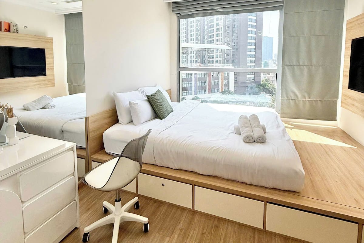 A modern hotel room with a large bed, a desk, a chair, and a TV.