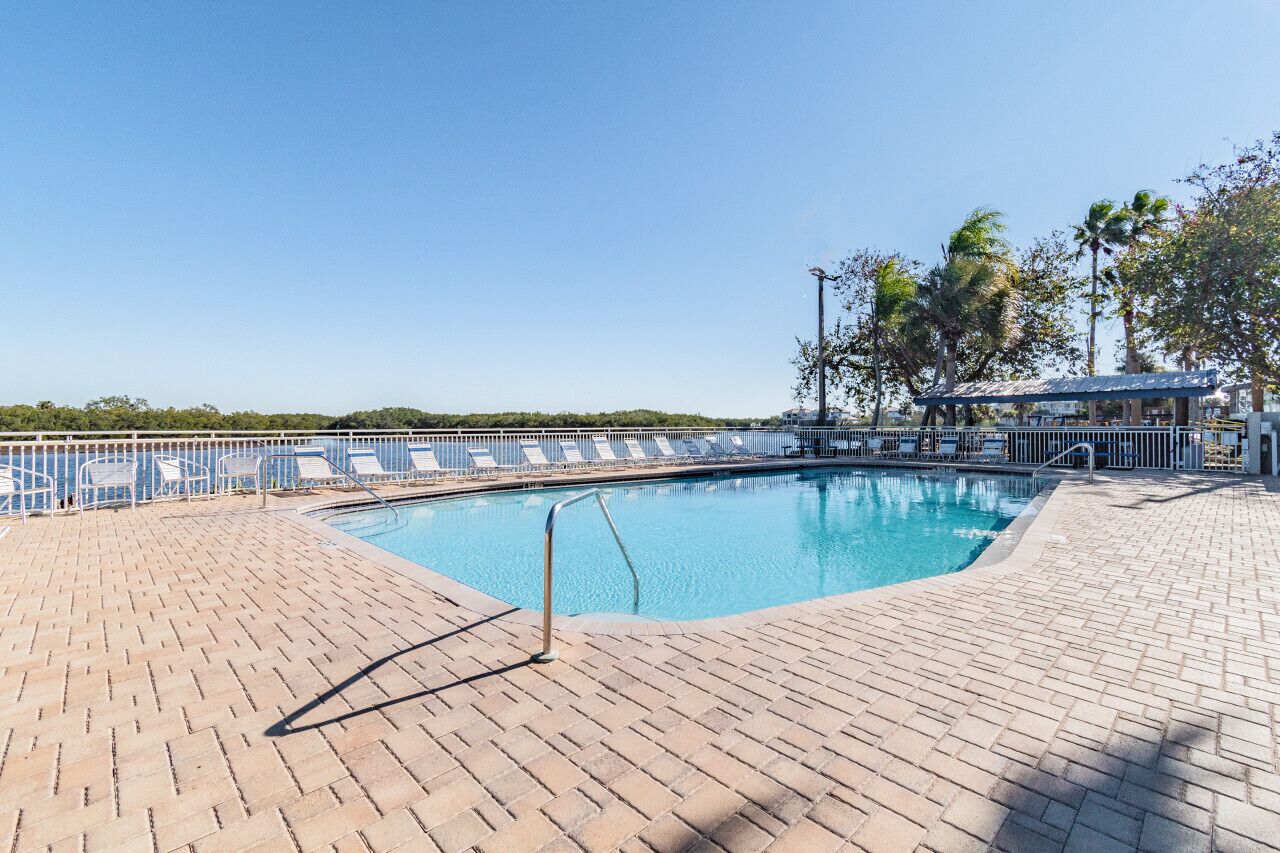 Una piscina rectangular con borde de baldosas, rodeada por una valla metálica y sillas de descanso.