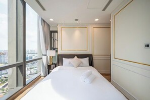 A hotel room with a large bed, a nightstand, a lamp, and a view of the city through large windows.