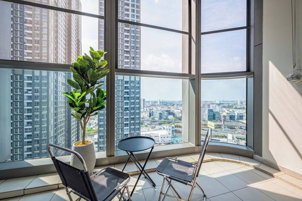 Un appartement situé dans un immeuble de grande hauteur, doté de grandes fenêtres, d’une plante en pot et de deux chaises.