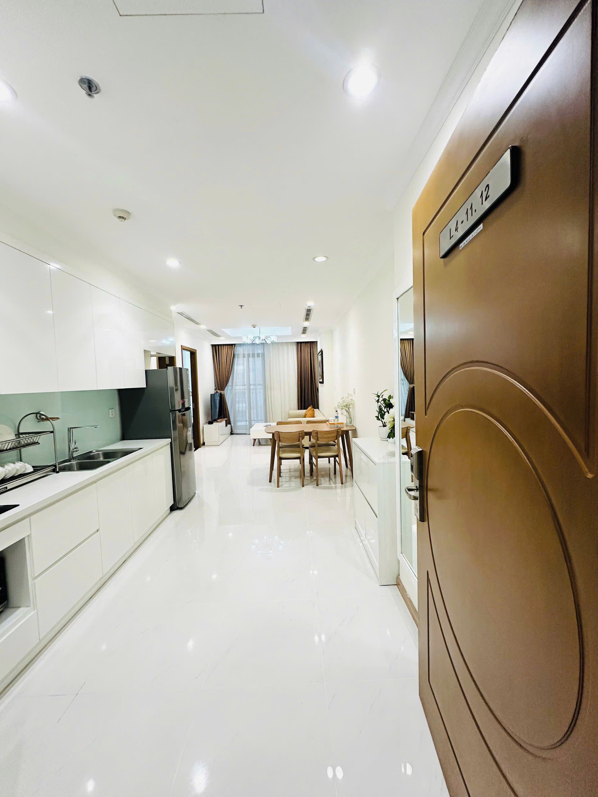 Una cocina moderna con armarios blancos, un refrigerador de acero inoxidable y un comedor con mesa y sillas de madera.