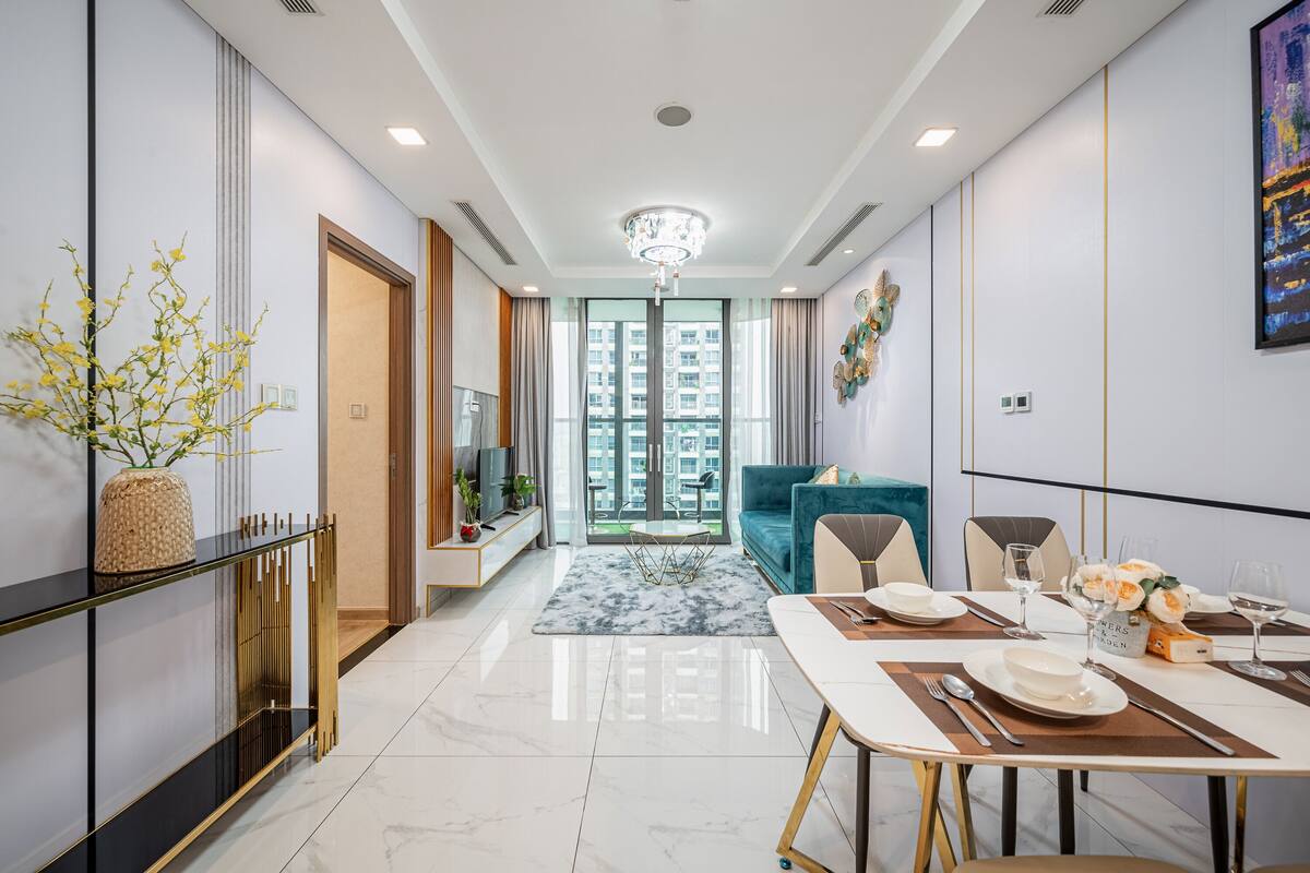 Un salon moderne avec un canapé, une table à manger pour quatre personnes et une grande fenêtre donnant sur des immeubles.