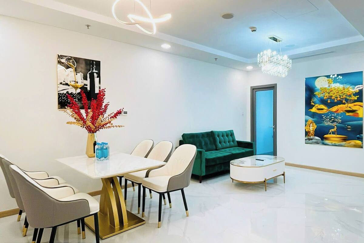 Un espace repas moderne avec une table et des chaises blanches, un canapé vert et un lustre.