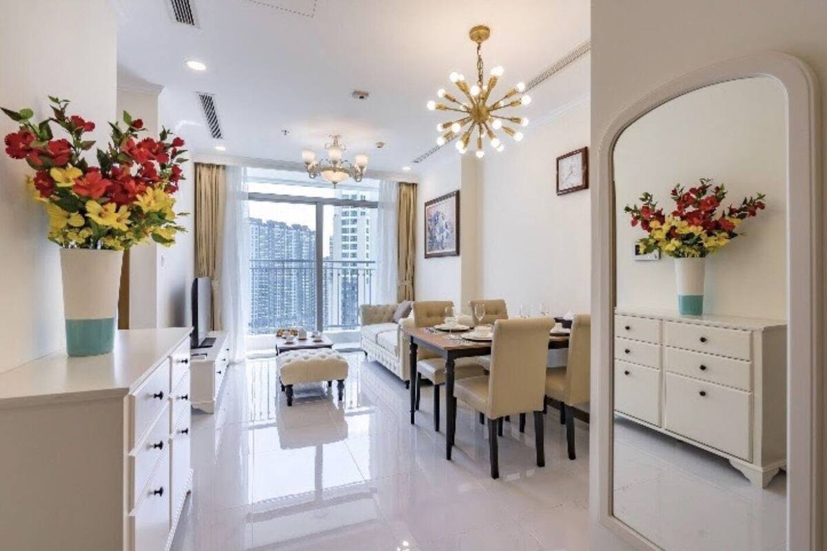 Un espace repas moderne avec une table blanche dressée pour quatre personnes, un canapé et un grand miroir.