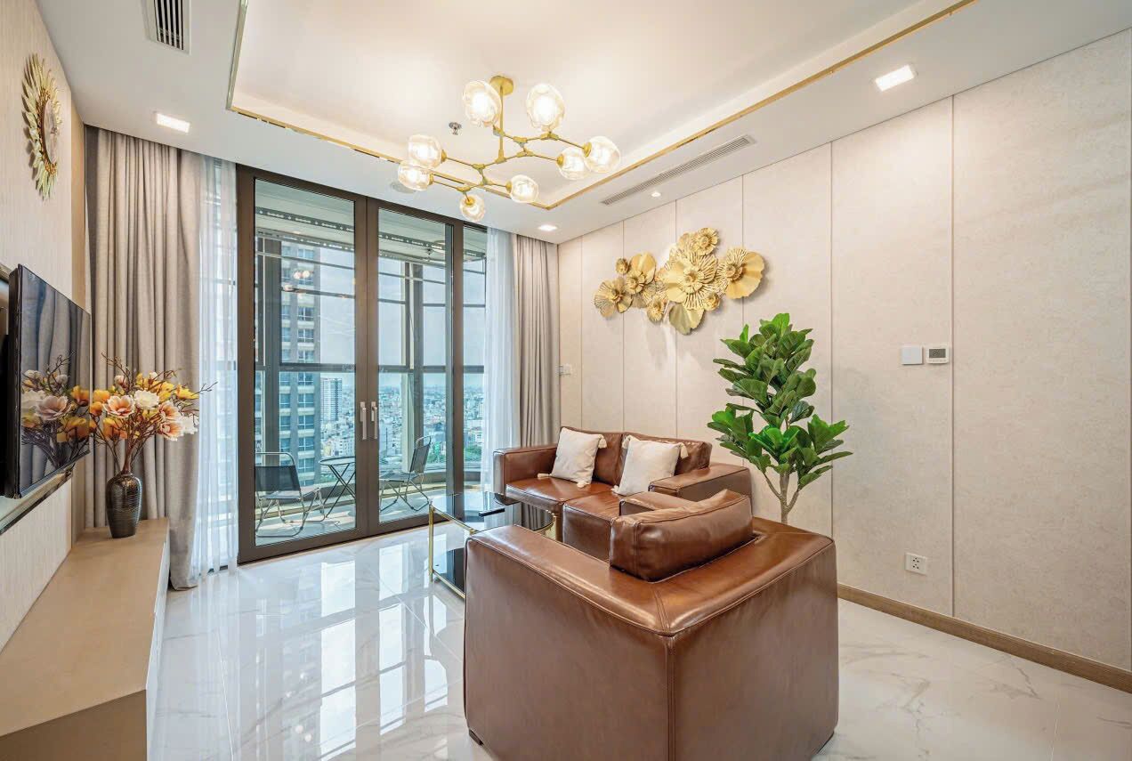 A modern living room with a brown leather sofa, a large window with a city view, a decorative wall piece, and a plant.