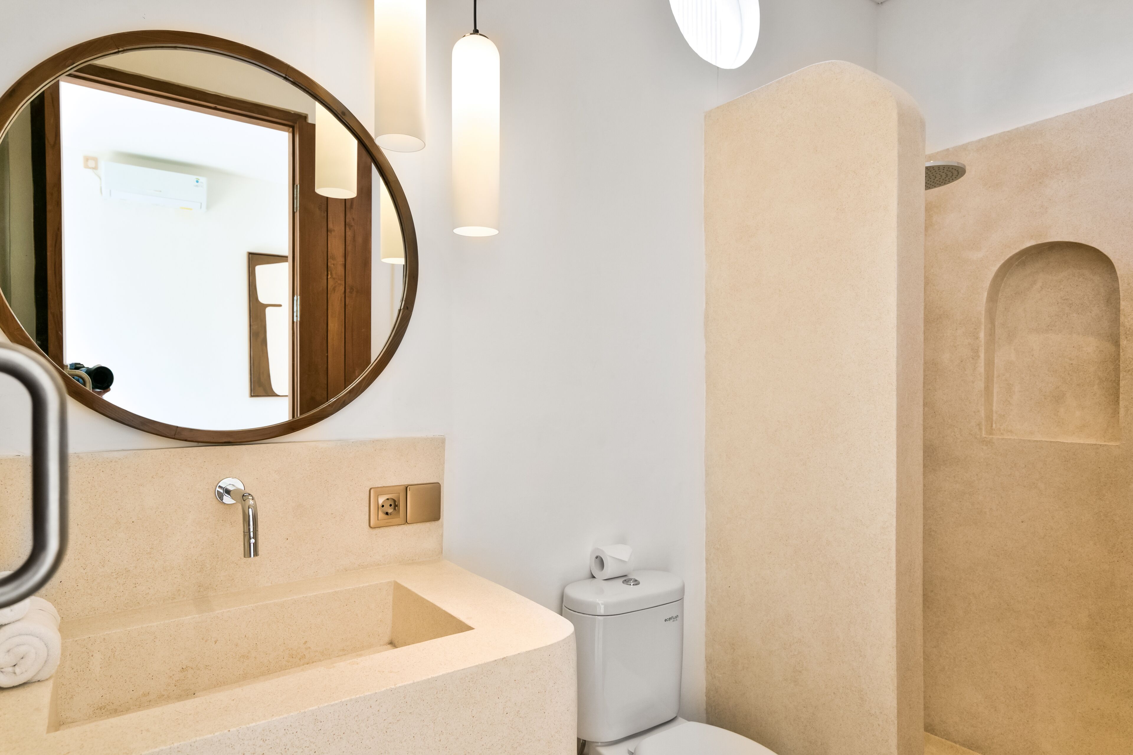 Ein Badezimmer mit rundem Spiegel, Waschbecken, Toilette und Duschbereich.