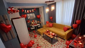 A living room with a sofa, a table with candles, and heart-shaped balloons. - EVLAND CİTY SUİT (Adana)