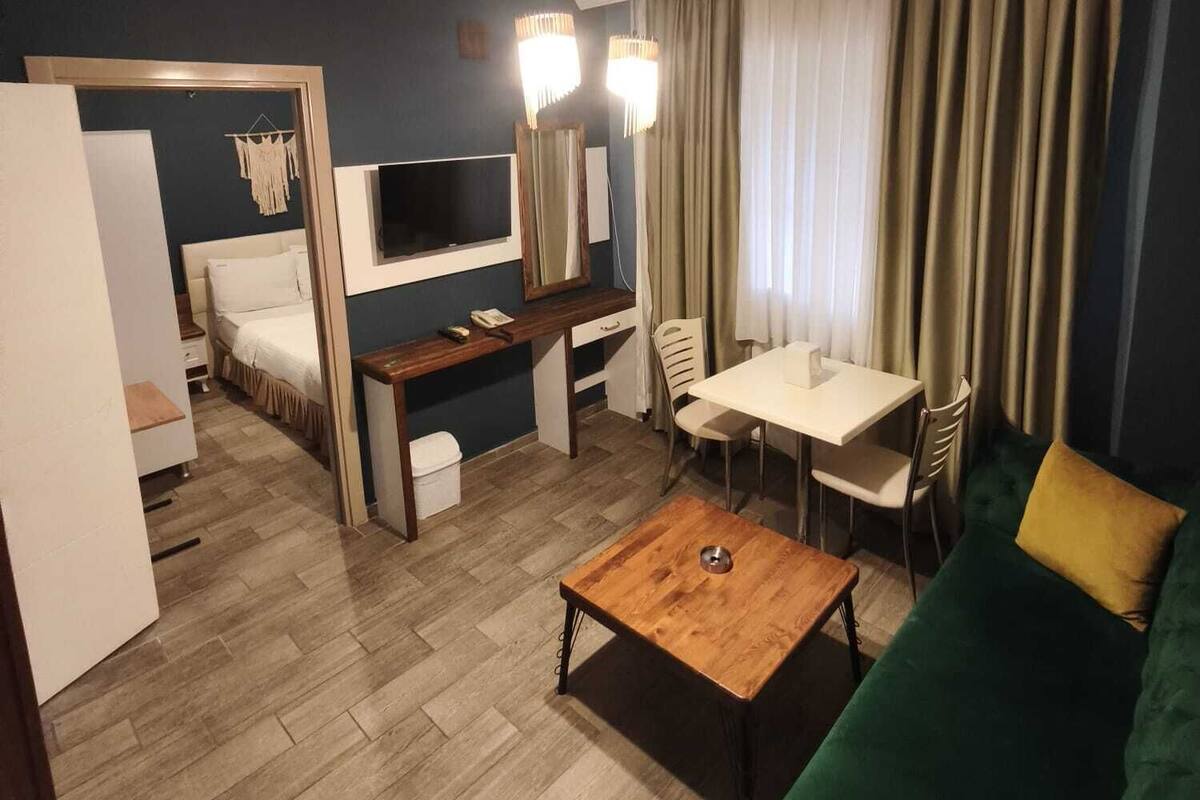 A modern hotel room with a bed, a desk, a TV, a dining area, and a green sofa.