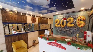 A reception area with a '2026' mural, a wooden reception desk, and a yellow chair. - EVLAND CİTY SUİT (Adana)