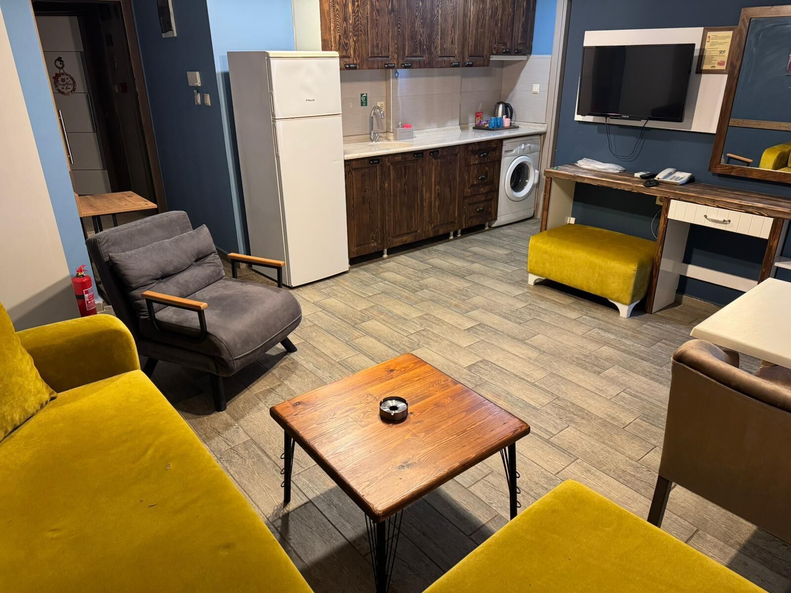 A compact living space with a sofa, a small table, a washing machine, a TV, and wooden cabinets.