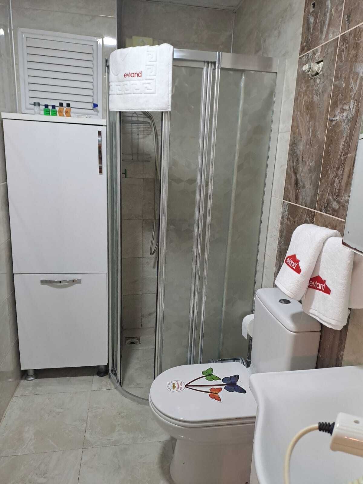 Een badkamer met een douchecabine van glas, een toilet met bloemenprint en een wit wastafel.