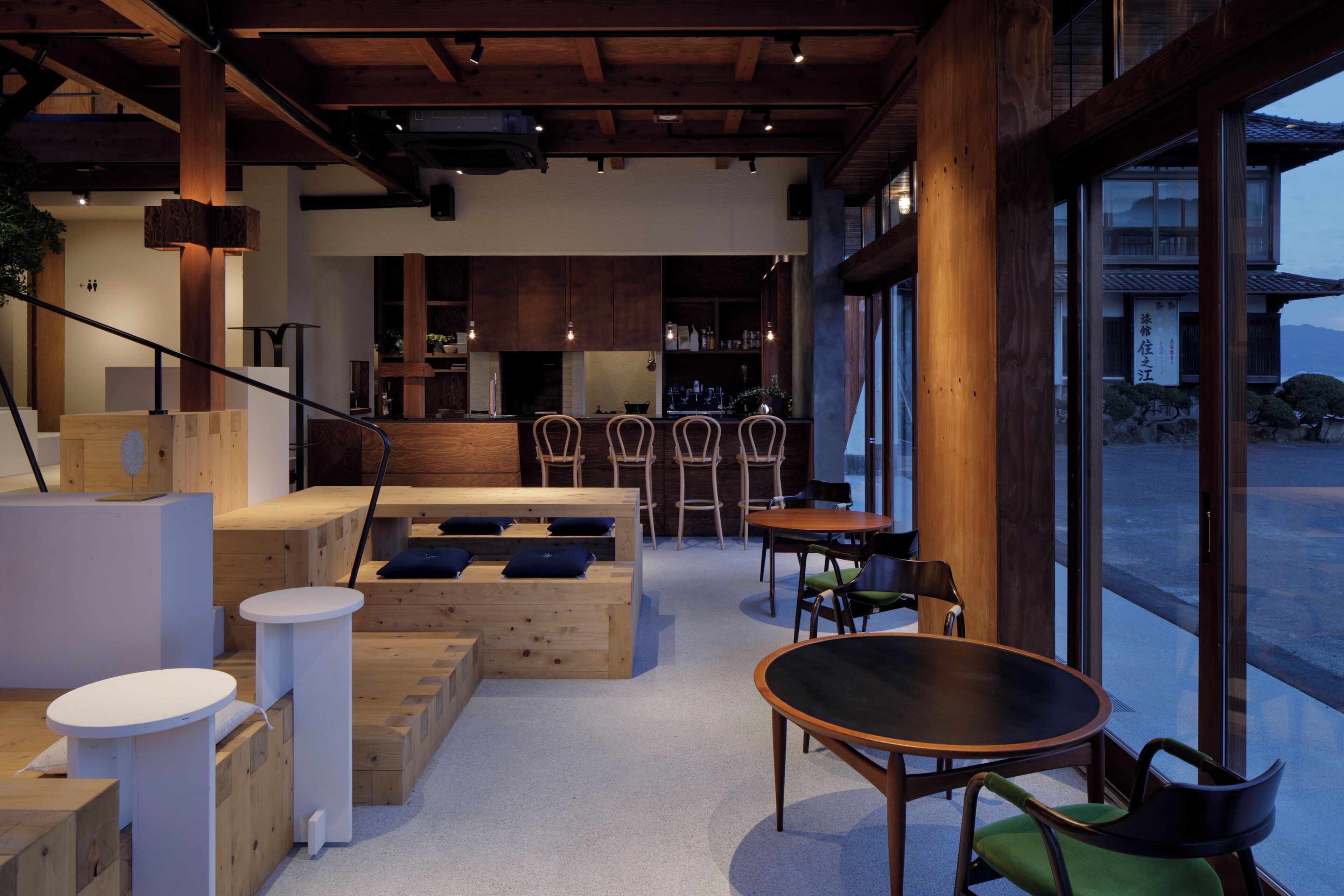 A modern interior with wooden furniture, a kitchen area, and large windows offering a view of the outdoors.