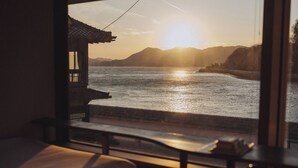 Una habitación con vista a un atardecer sobre el agua, una estructura de madera y un banco.
