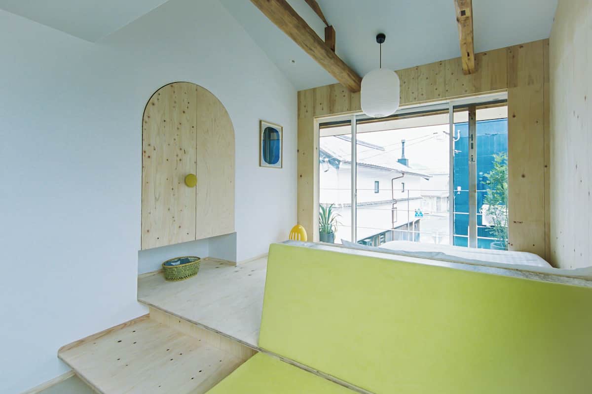 A room with a wooden ceiling, a large window, a green sofa, and a small table with a basket.