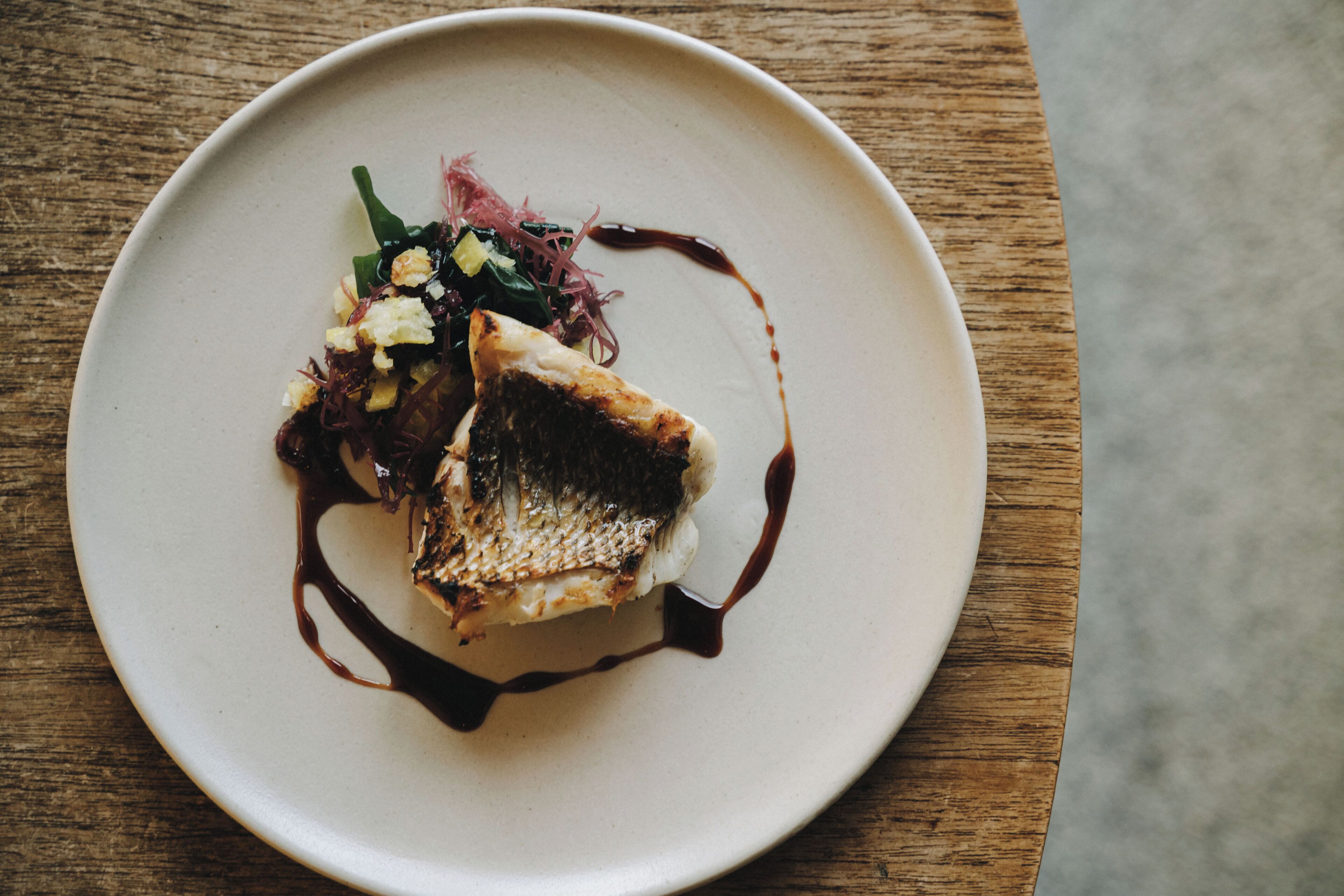 A plate with a piece of fish, some greens, and a sauce.