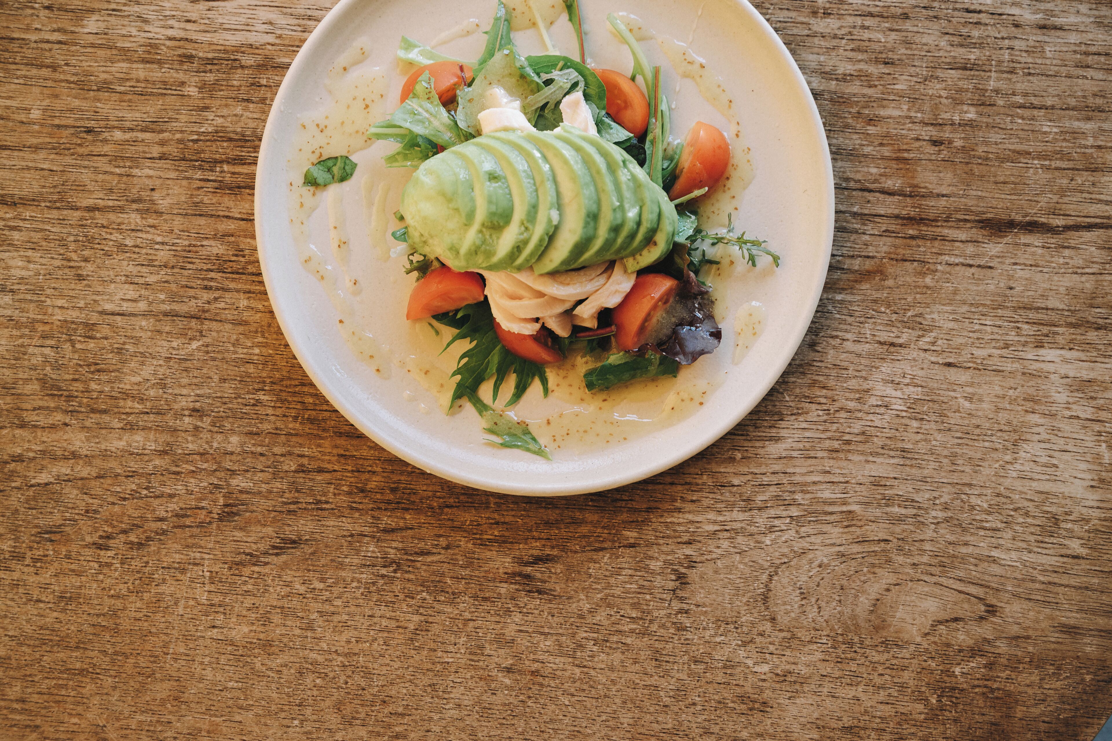 A plate of food with a variety of vegetables and a slice of avocado on a wooden table.
