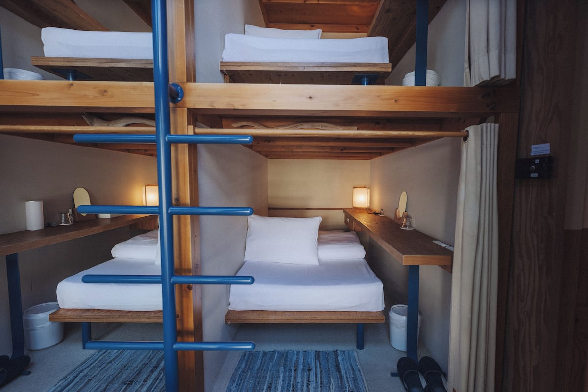 A bunk bed room with a wooden ladder, a desk with a lamp, and a small rug.
