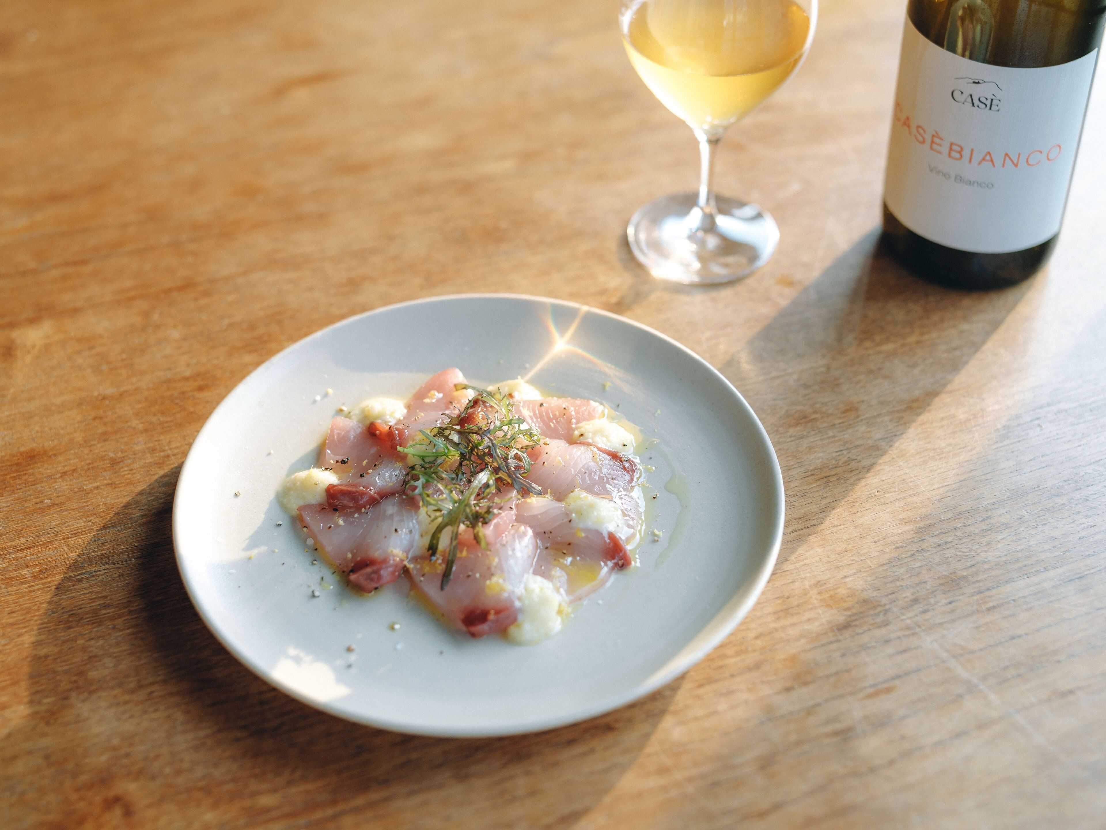 A plate of food with a glass of white wine and a bottle of wine on a wooden table.