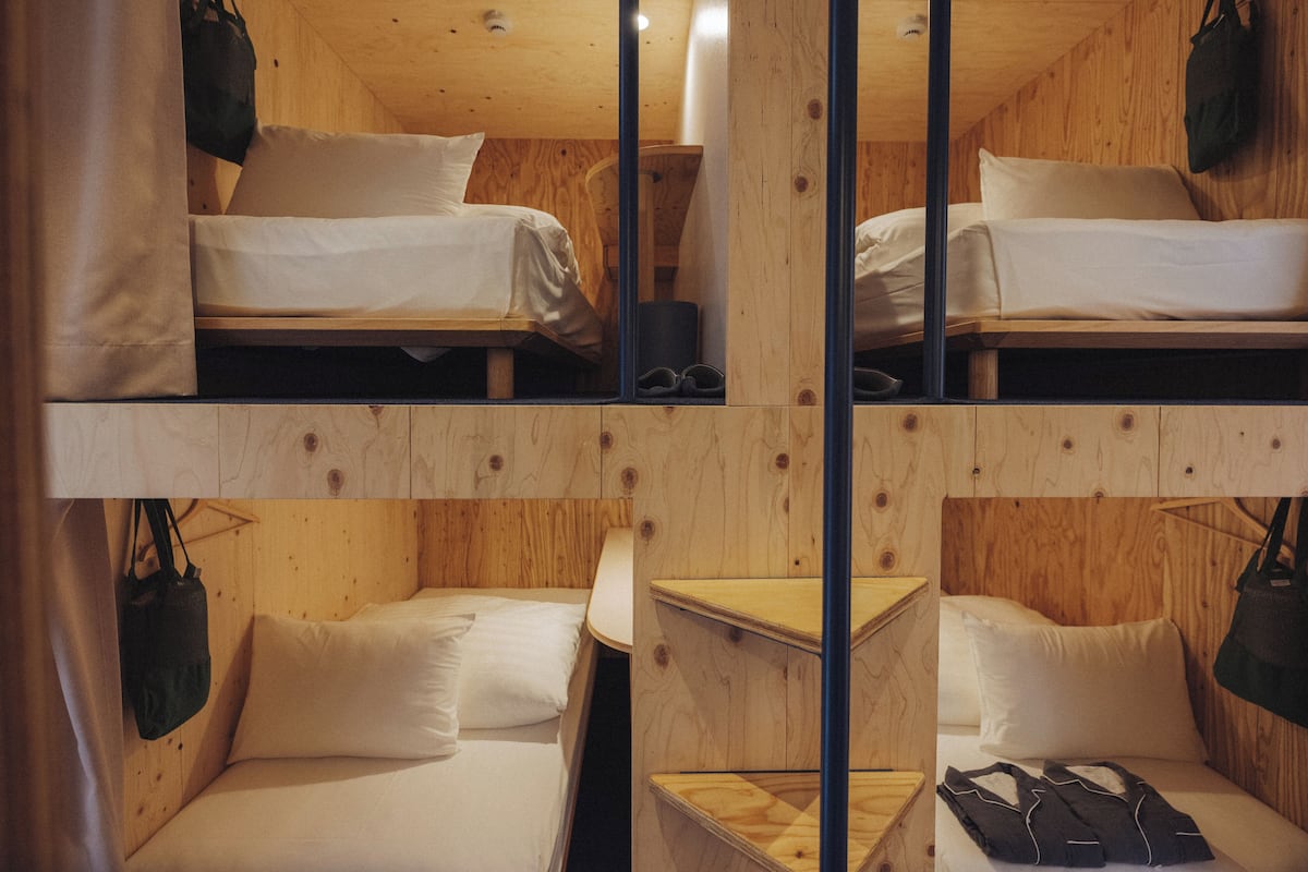 A room with two bunk beds and a single bed, wooden walls, and hanging bags.