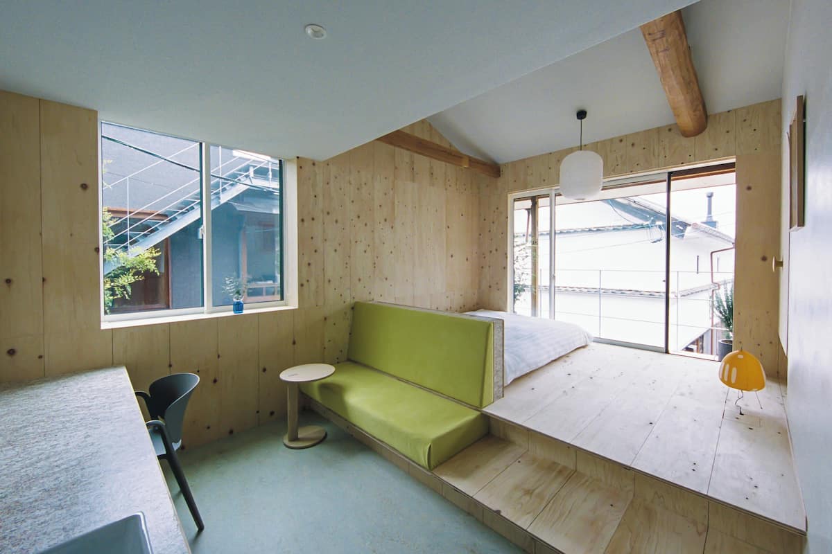 A room with a green sofa, a small round table, and a large window with a view of buildings outside.