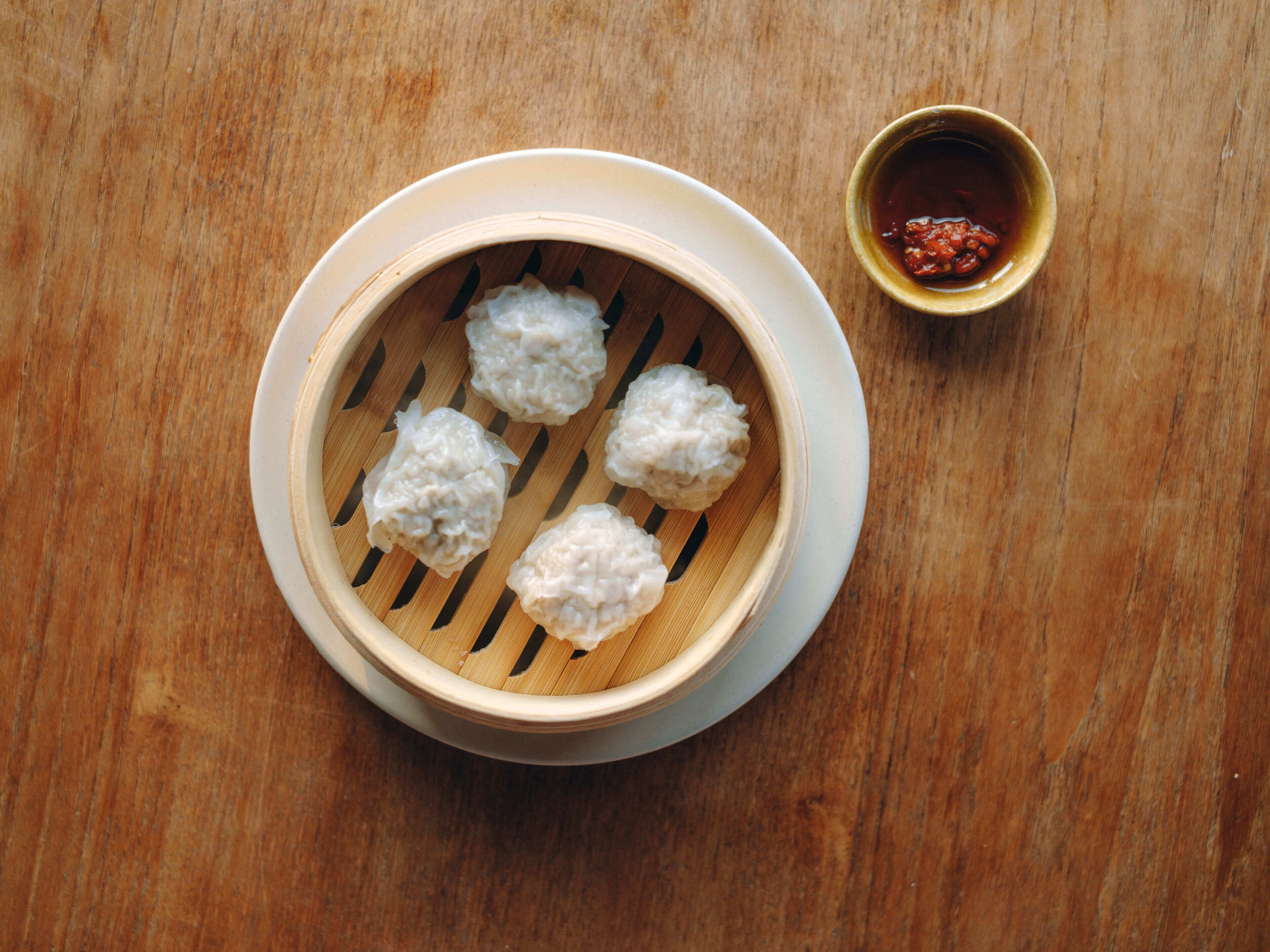 A bamboo steamer with dumplings on a wooden table.
