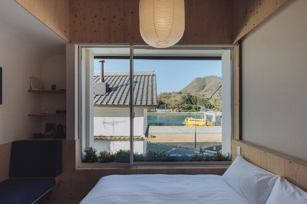 A bedroom with a large window, wooden ceiling, and a bed with white bedding.
