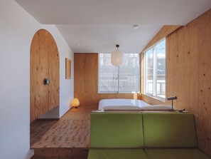 Ein modernes Zimmer mit Holzwänden, einem großen Fenster, einem grünen Sofa und einer hängenden Leuchte.