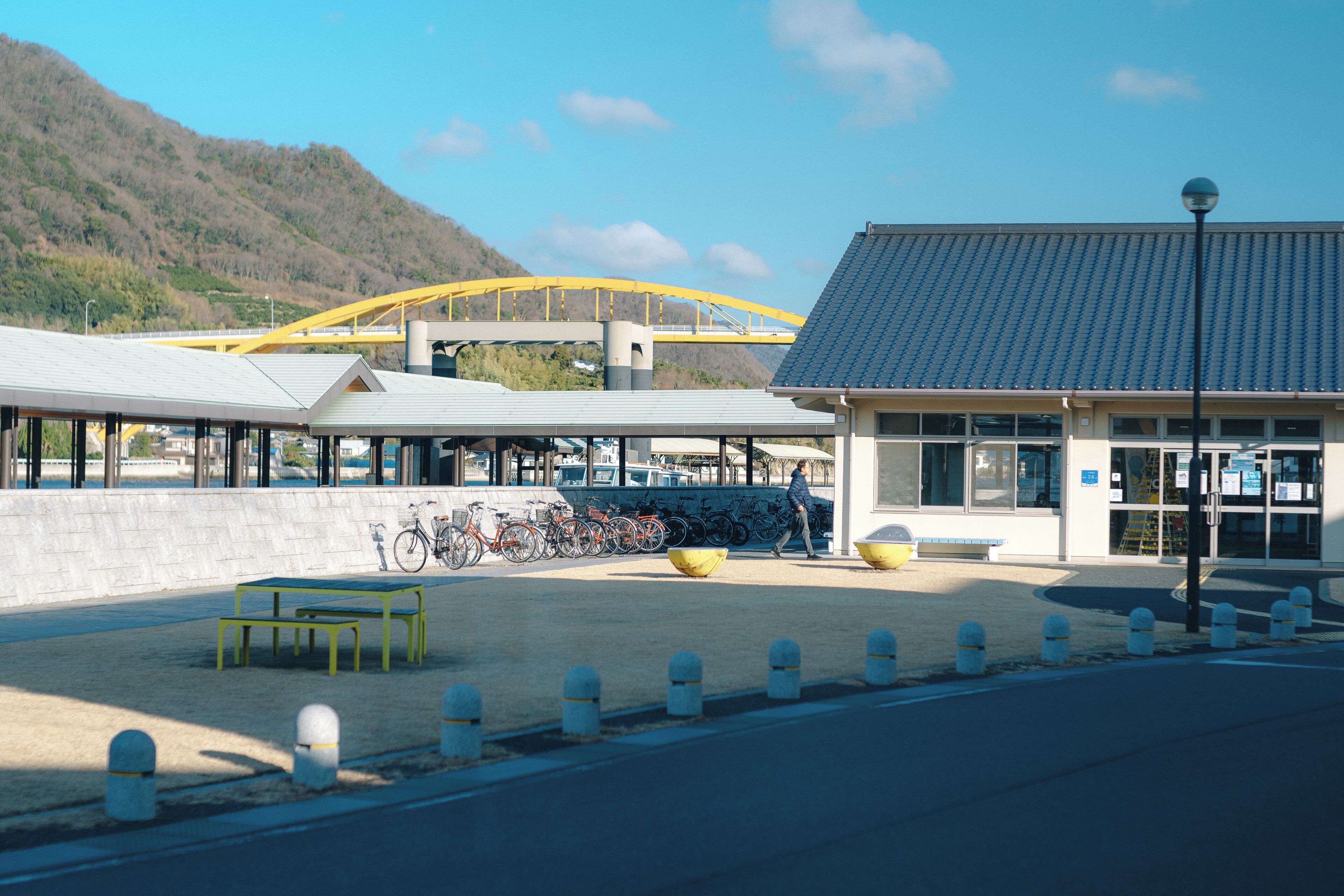 A building with a tiled roof, a covered outdoor area with benches, and a bicycle parking area.