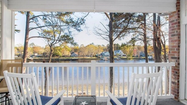 A covered porch with white railings and two white chairs with blue cushions. - Cozy two Bedroom Apartment at Riverwalk At Arrowhead (Myrtle Beach)