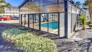 A modern glass-enclosed structure with a pool, surrounded by landscaped areas and palm trees. - Cozy two Bedroom Apartment at Riverwalk At Arrowhead (Myrtle Beach)