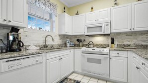 A kitchen with white cabinets, a microwave, a stove, and a coffee maker. - Cozy two Bedroom Apartment at Riverwalk At Arrowhead (Myrtle Beach)