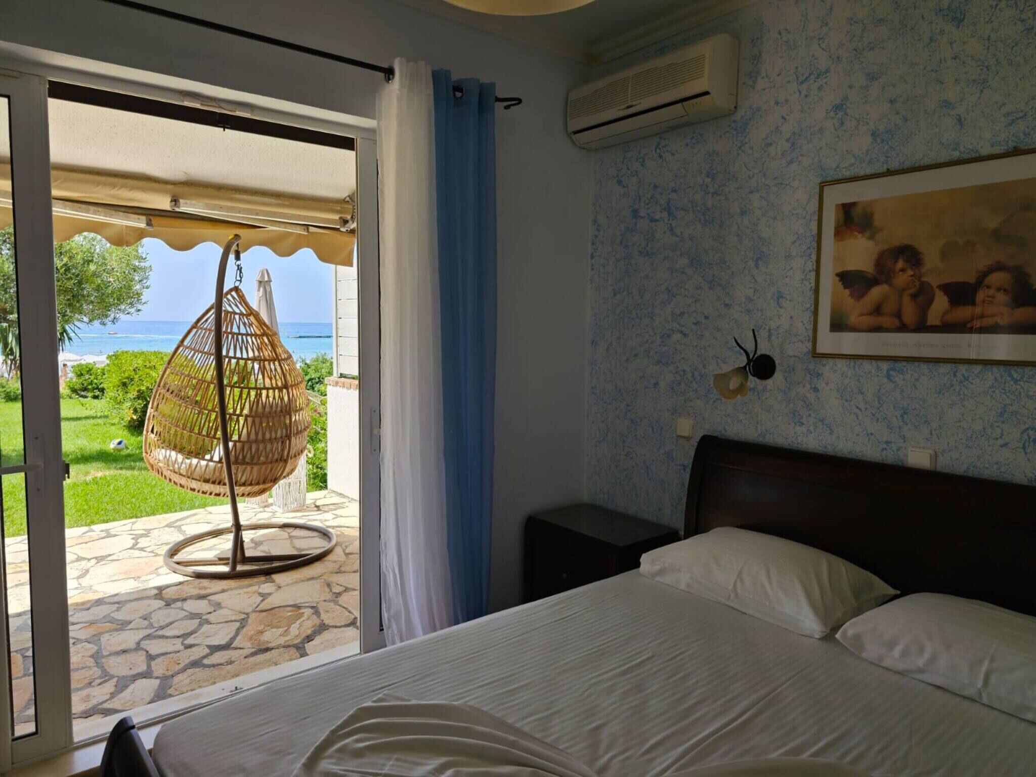 A bedroom with a bed, a hanging chair, a view of the sea, and a painting on the wall.