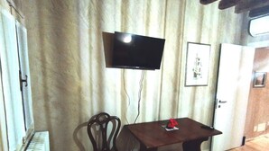 Ett rum med ett träbord, en stol, en tv som är monterad på väggen och en dörr.