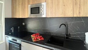 A modern kitchen with a built-in microwave, black marble countertop, and wooden cabinets. - Modern Apartment With sea View (Podstrana)