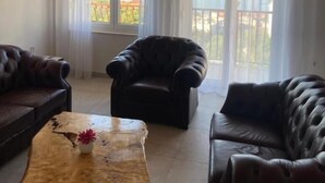 A room with a wooden ceiling, two leather sofas, a wooden coffee table with a flower vase, and a view of the sea through large windows with sheer curtains. - Modern Apartment With sea View (Podstrana)