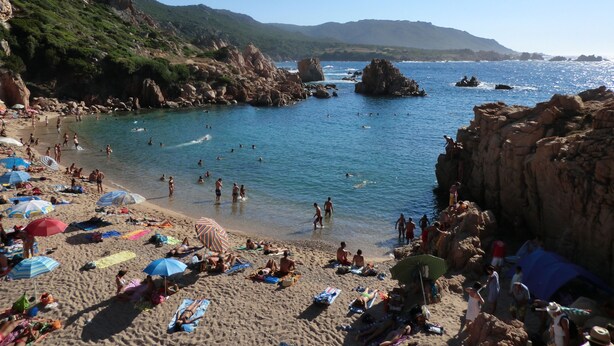 A beach with people sunbathing, swimming, and walking along the shore.