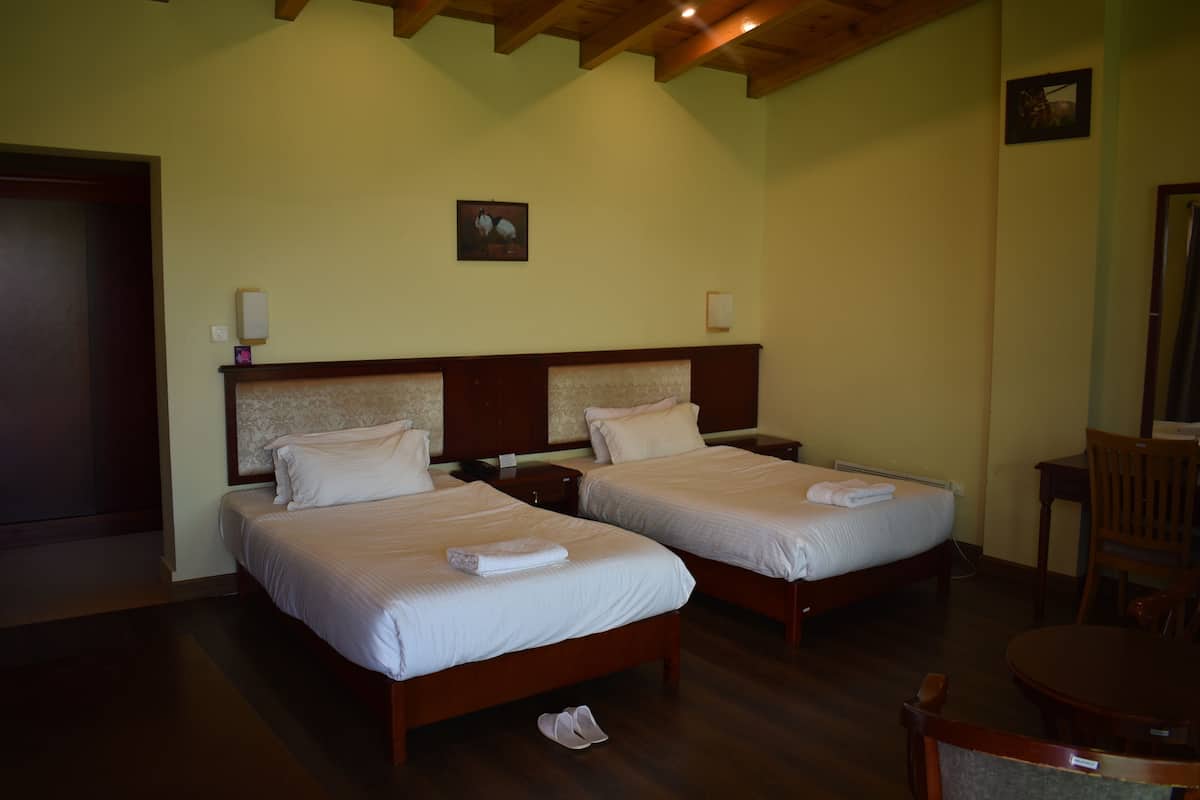 A hotel room with two beds, wooden headboards, a small table, and a chair.