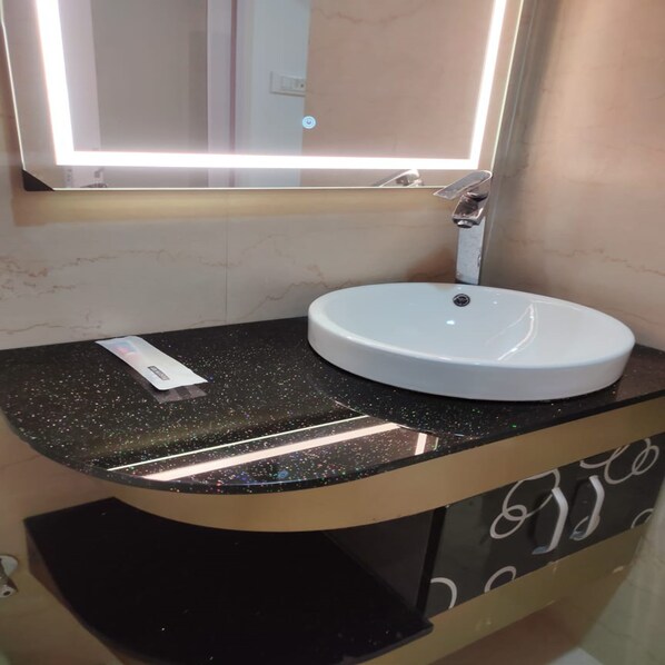 A bathroom with a round white sink, a black countertop with a speckled pattern, and a mirror above the sink. - Hotel Hindustan Inn (Rairangpur)