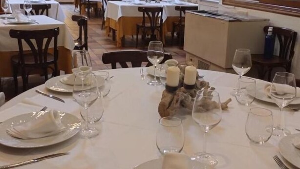 Un restaurant où les tables rondes sont dressées pour le repas, avec des nappes blanches et une disposition soignée des assiettes, des verres et des couverts.