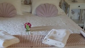 Un lit bien fait, agrémenté d’une rose rose, d’une serviette blanche et d’une serviette pliée, le tout sur un fond de papier peint à motifs floraux.