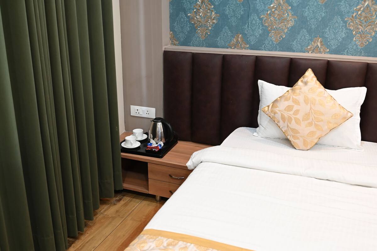 Ein Hotelzimmer mit einem Bett, einem Nachttisch mit Wasserkocher, Tassen und einem Tablett sowie einem Vorhang.