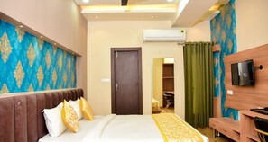 A hotel room with a bed, a TV, a wardrobe, and an air conditioning unit. - Hotel Olive Crown (Lucknow)
